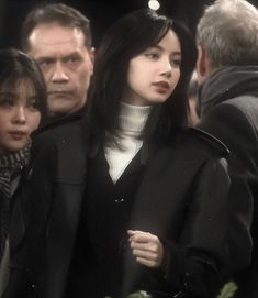 a woman in black coat and white turtle neck sweater walking with other people behind her