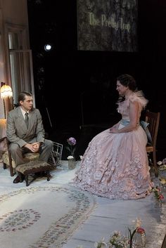 a man and woman sitting on chairs in front of a stage with flowers around them