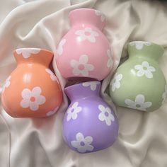 four ceramic vases sitting on top of a white cloth covered bedding with flowers painted on them