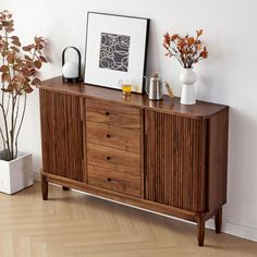 a wooden cabinet with two vases on top of it next to a potted plant