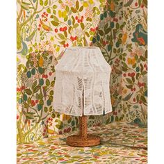 a table lamp with a white lace shade on it's base in front of a floral wallpaper