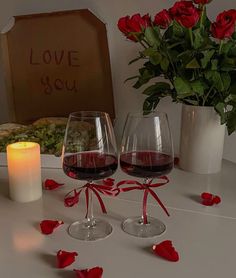 two glasses of red wine on a table with roses