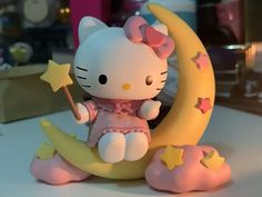 a hello kitty figurine sitting on the moon holding a star in her hand