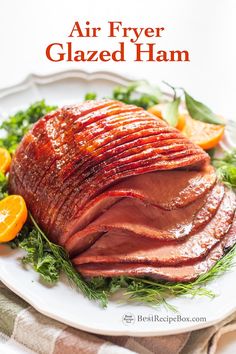 an air fryer glazed ham on a white plate with oranges and herbs around it