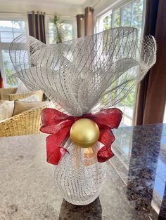 a glass vase with a red bow and a golden ornament in it on a table