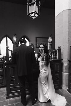 a woman in a wedding dress standing next to a man holding a cell phone up to her face