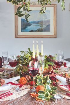 The table is set for a seasonal celebration, with a naturalistic arrangement of holly branches, fir cones and festive oranges, and each place simply marked with a napkin tied with a red ribbon, holly leaves and a fir cone.