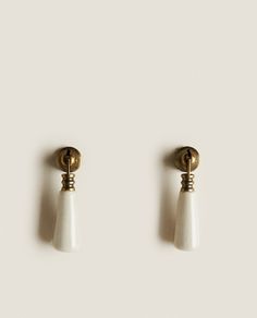 two white and gold earrings on a white surface with one earring in the shape of a cone