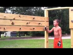 a young man standing next to a wooden structure with climbing ropes on it's sides