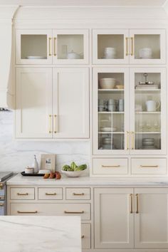 a kitchen with white cabinets and marble counter tops, gold pulls on the cupboards