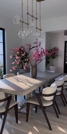 a dining room table and chairs with flowers in vases on the top one side