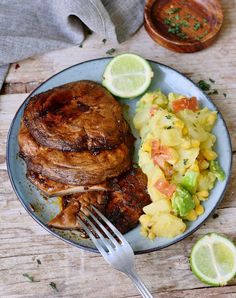 a plate with meat, pineapple salad and lime wedges next to a fork