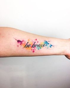 a woman's arm with the words be brave painted on it and watercolor splashs