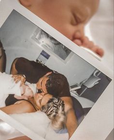 a baby laying on top of a bed next to an adult holding a polaroid