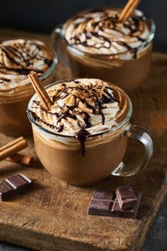 two cups of hot chocolate with marshmallows and cinnamon sticks on the side