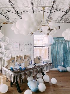 a room filled with lots of white and blue balloons hanging from the ceiling next to a table