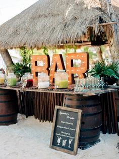 an outdoor bar set up on the beach with drinks in jars and glasses sitting on top of barrels