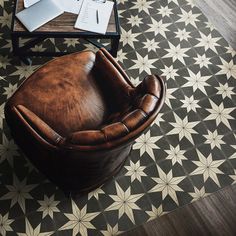 a brown leather chair sitting on top of a black and white floor next to a table