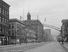 an old black and white photo of a city street with buildings on both sides that have arches over them