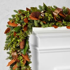 a christmas wreath with pine cones and greenery hanging from the front of a white fireplace