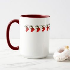 a white and red coffee mug with christmas stockings on it next to a donut