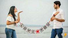 a man and woman standing next to each other on the beach holding a banner that says i love you