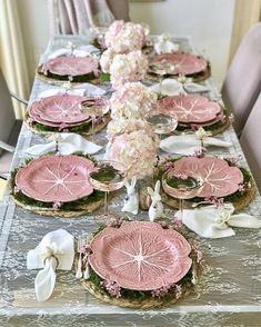 a long table with pink plates and flowers on it is set for a formal dinner