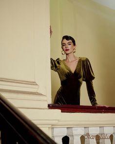 a woman in a green dress is standing on the stairs with her hands behind her head