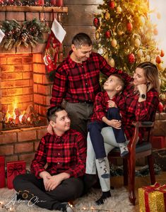 a man and two women are sitting next to a christmas tree with their children in matching plaid shirts