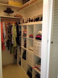 an organized closet with white shelving and lots of clothes hanging on the shelves in front of it