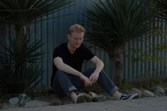 a man sitting on the ground in front of palm trees