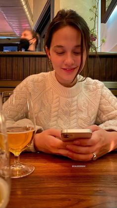 a woman sitting at a table looking at her cell phone while holding a glass of wine