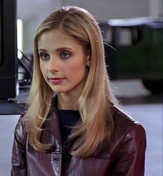 a woman with long blonde hair wearing a brown leather jacket and looking at the camera