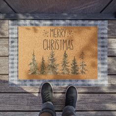 a person standing in front of a merry christmas door mat with pine trees on it