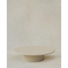 a round white table sitting on top of a cement floor next to a beige wall