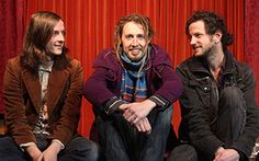 three men sitting next to each other in front of red curtains