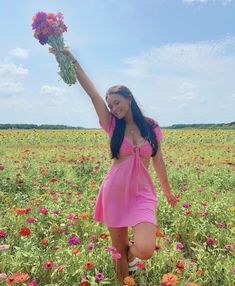 a woman in a pink dress is holding flowers and standing in a field full of flowers