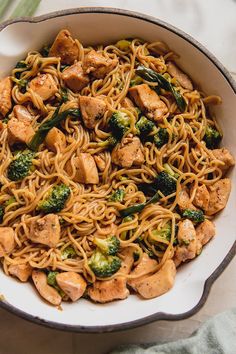 a white bowl filled with chicken and broccoli stir - frying on top of a table