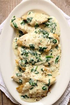 a white plate topped with ravioli and spinach covered in cheese sauce on top of a wooden table