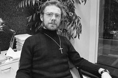 a man with glasses sitting in front of a desk next to a potted plant