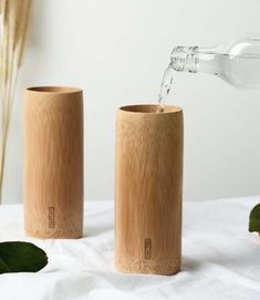 two wooden vases sitting on top of a white sheet next to a bottle of water