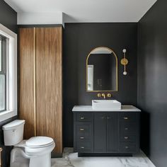 a white toilet sitting next to a sink in a bathroom under a mirror and a wooden cabinet