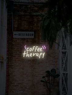 a neon sign that reads coffee therapy on the side of a brick wall next to a potted plant