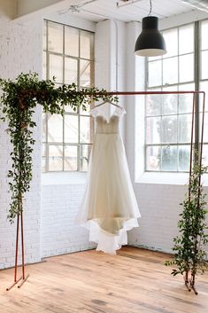 a wedding dress hanging on a rack in front of a window with potted plants