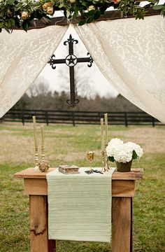 a wooden table topped with a cross and flowers next to a white cloth draped over it