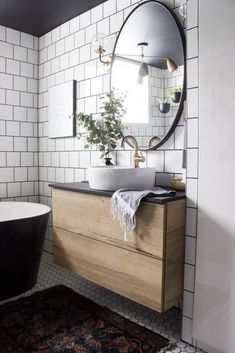 a black and white bath tub sitting next to a sink in a bathroom under a round mirror