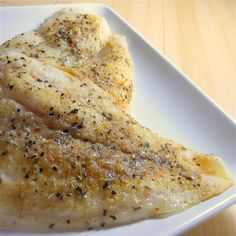 two pieces of chicken on a white plate with seasoning sprinkled over them