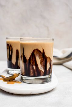 two glasses filled with liquid sitting on top of a white plate