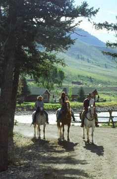 three people riding horses down a dirt road