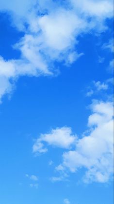 the airplane is flying high in the blue sky with fluffy white clouds above it,